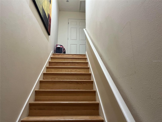 staircase with wood finished floors and a textured wall