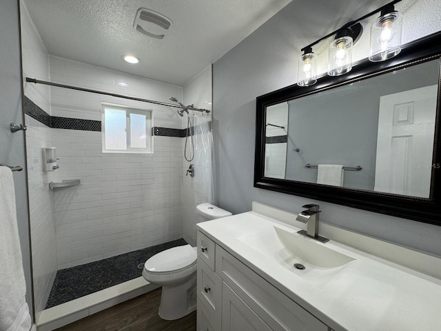 bathroom featuring a textured ceiling, hardwood / wood-style floors, vanity, toilet, and a tile shower