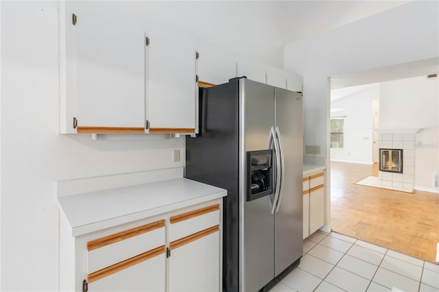 kitchen featuring white cabinetry, stainless steel fridge, a tiled fireplace, and light tile patterned floors