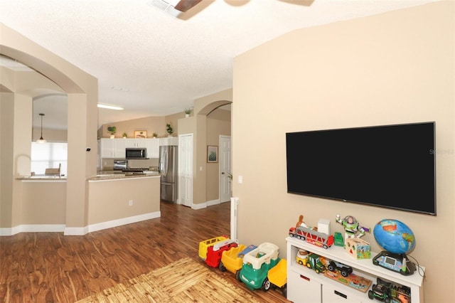 game room featuring lofted ceiling, dark wood-type flooring, a textured ceiling, and ceiling fan