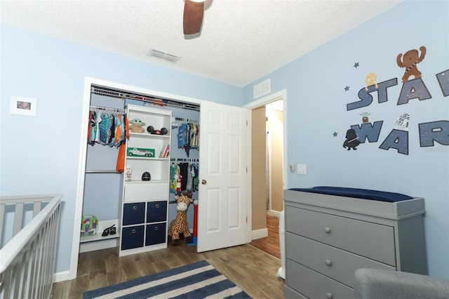 bedroom with a nursery area, dark hardwood / wood-style floors, a textured ceiling, and a closet