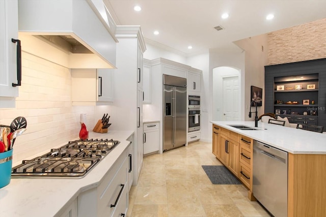 kitchen with white cabinetry, stainless steel appliances, sink, premium range hood, and a center island with sink