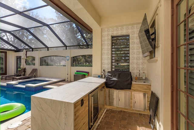 interior space featuring glass enclosure, a swimming pool with hot tub, exterior kitchen, a grill, and beverage cooler