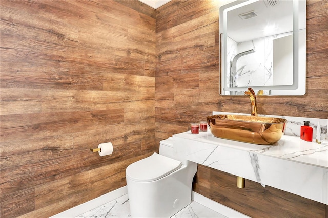 bathroom featuring sink, wooden walls, and toilet