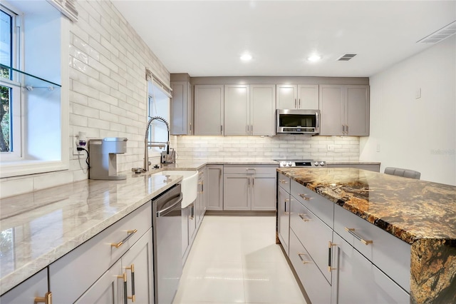 kitchen featuring stainless steel appliances, gray cabinets, and light stone counters