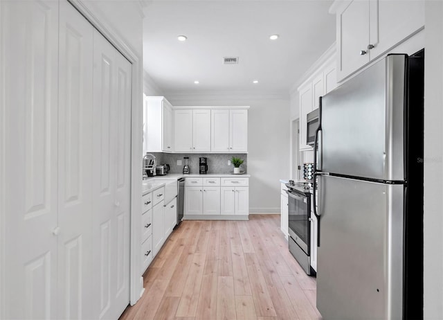 kitchen with light hardwood / wood-style flooring, appliances with stainless steel finishes, white cabinets, tasteful backsplash, and ornamental molding