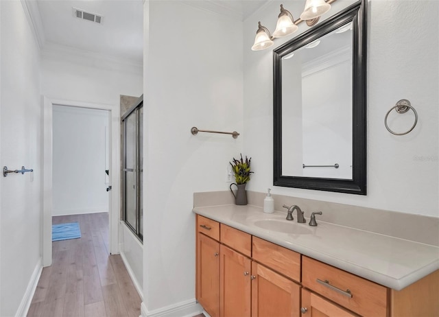 bathroom featuring wood-type flooring, bath / shower combo with glass door, vanity, and ornamental molding