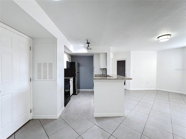 kitchen with a textured ceiling, black fridge, white cabinets, light tile patterned flooring, and dark stone counters