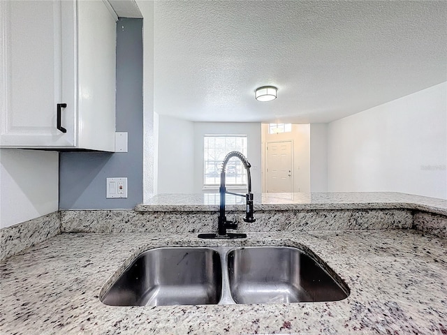 kitchen featuring light stone countertops, sink, white cabinets, and a textured ceiling