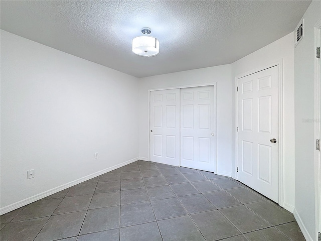 unfurnished bedroom with dark tile patterned flooring, a closet, and a textured ceiling