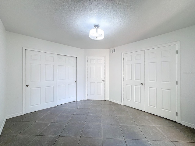 unfurnished bedroom featuring a textured ceiling and dark tile patterned floors