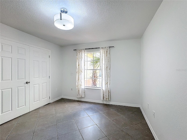 unfurnished bedroom featuring a textured ceiling, a closet, and dark tile patterned floors