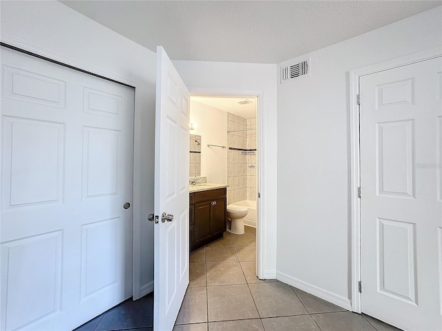 bathroom featuring tile patterned flooring, vanity, tiled shower, toilet, and a textured ceiling