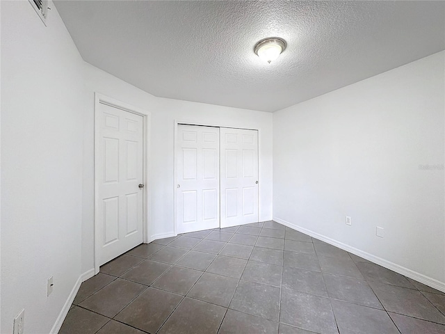 unfurnished bedroom featuring a textured ceiling, a closet, and dark tile patterned floors