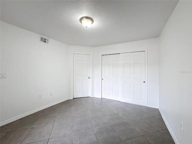 unfurnished bedroom with dark tile patterned flooring, a closet, and a textured ceiling