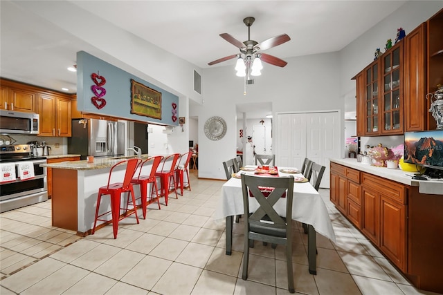 kitchen with a breakfast bar area, ceiling fan, stainless steel appliances, light stone counters, and an island with sink