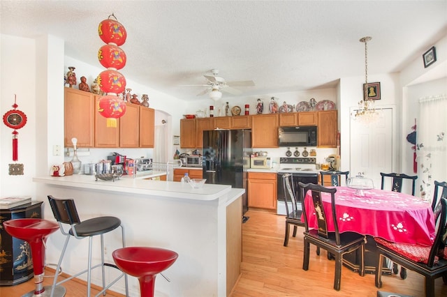 kitchen with ceiling fan, hanging light fixtures, light hardwood / wood-style floors, black appliances, and kitchen peninsula