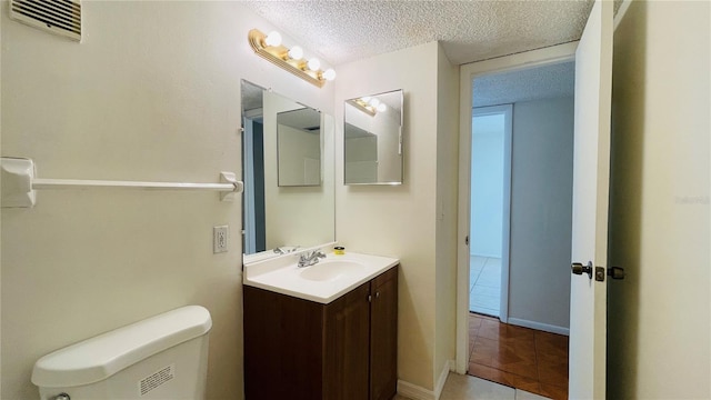 bathroom featuring vanity, toilet, tile patterned floors, and a textured ceiling