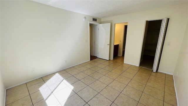 unfurnished bedroom featuring light tile patterned flooring, a textured ceiling, a closet, and a spacious closet