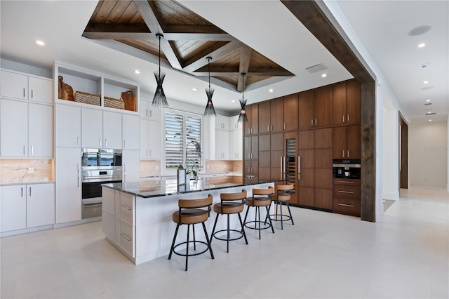 kitchen with pendant lighting, white cabinetry, decorative backsplash, a kitchen island with sink, and stainless steel double oven