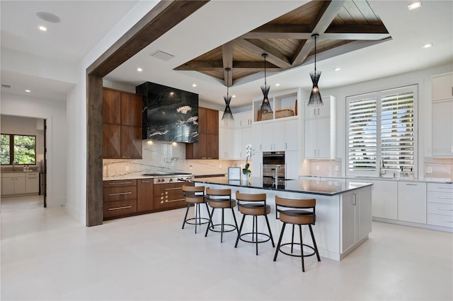 kitchen featuring ventilation hood, white cabinetry, pendant lighting, and a center island with sink