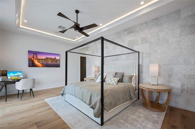 bedroom featuring a raised ceiling, ceiling fan, and light wood-type flooring