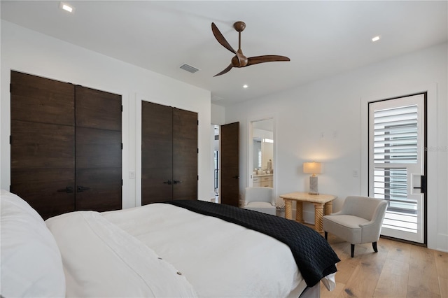 bedroom featuring two closets, ensuite bathroom, ceiling fan, and light wood-type flooring