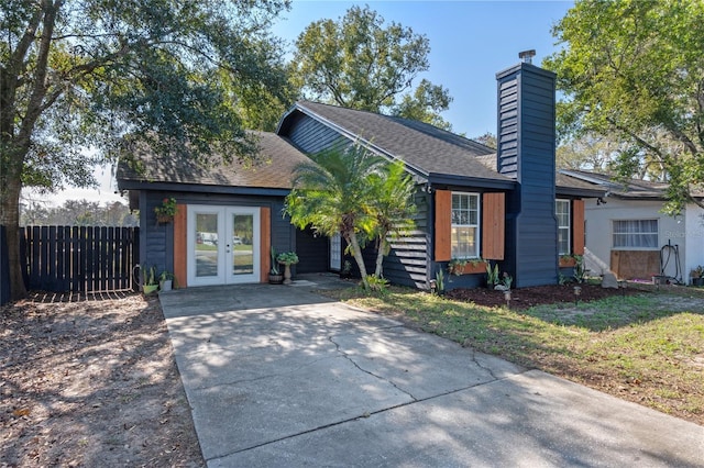 view of front of property featuring fence, roof with shingles, a chimney, concrete driveway, and french doors