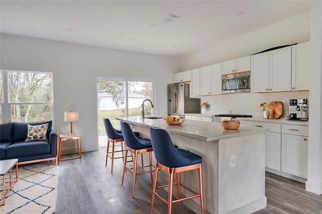 kitchen with appliances with stainless steel finishes, sink, white cabinets, hardwood / wood-style flooring, and a center island with sink