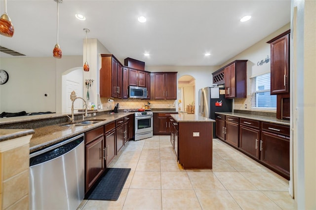 kitchen with sink, appliances with stainless steel finishes, tasteful backsplash, a kitchen island, and decorative light fixtures