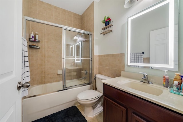 full bathroom with tile patterned floors, toilet, bath / shower combo with glass door, tile walls, and vanity