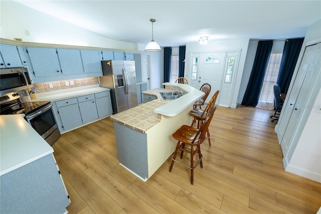 kitchen with sink, appliances with stainless steel finishes, tasteful backsplash, light hardwood / wood-style floors, and decorative light fixtures