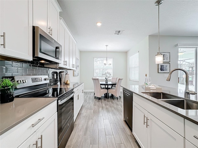 8886 Fallen Oak Dr, Davenport, FL 33896 - kitchen with stainless steel appliances, white cabinetry, light wood-style flooring, hanging light fixtures, and a textured ceiling