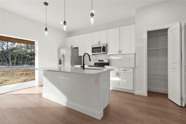 kitchen featuring stainless steel appliances, hanging light fixtures, backsplash, white cabinets, and a kitchen island with sink