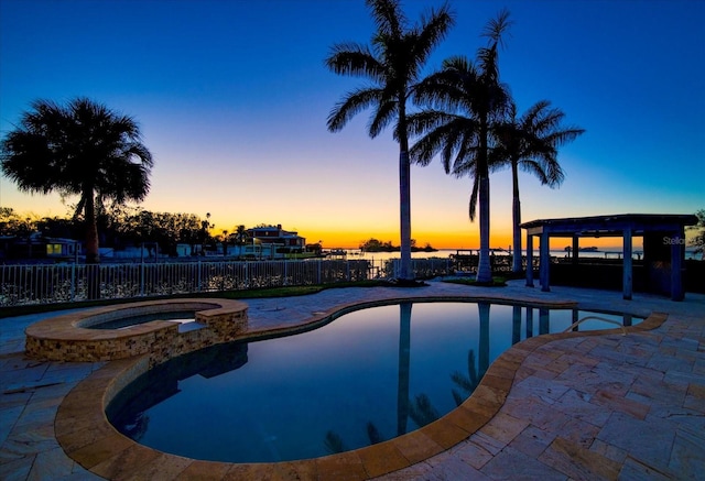 pool at dusk with an in ground hot tub and a patio