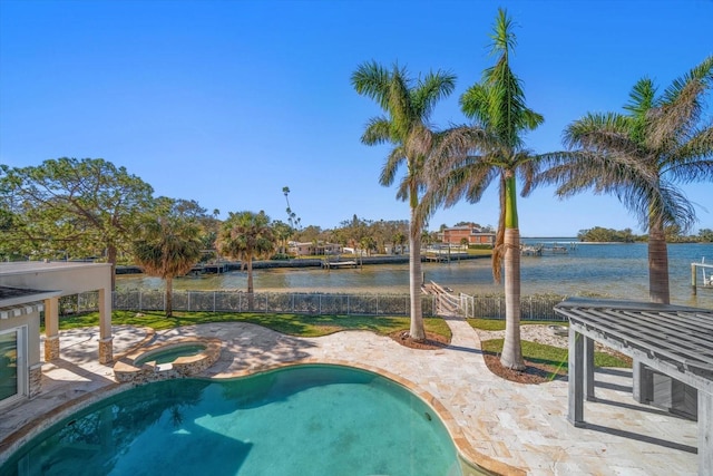 pool with an in ground hot tub, a patio, a water view, and fence