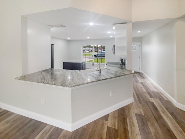 kitchen with sink, light stone counters, wood-type flooring, white cabinets, and kitchen peninsula