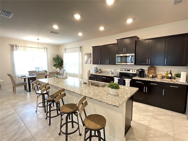 kitchen with appliances with stainless steel finishes, an island with sink, sink, hanging light fixtures, and a breakfast bar area