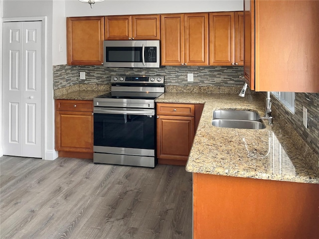 kitchen with appliances with stainless steel finishes, decorative backsplash, sink, dark hardwood / wood-style floors, and light stone counters