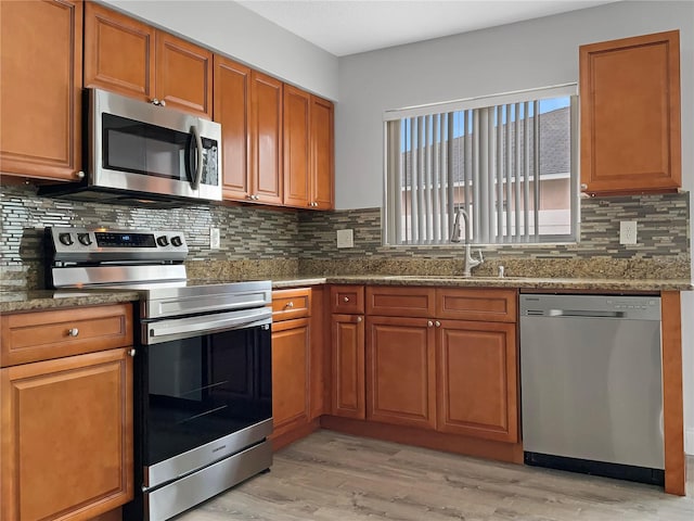 kitchen with stainless steel appliances, light hardwood / wood-style floors, sink, stone countertops, and backsplash