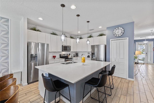 kitchen featuring white cabinets, stainless steel appliances, sink, a kitchen island with sink, and a breakfast bar