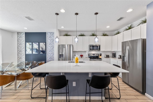 kitchen featuring decorative light fixtures, a kitchen island with sink, a kitchen breakfast bar, and appliances with stainless steel finishes