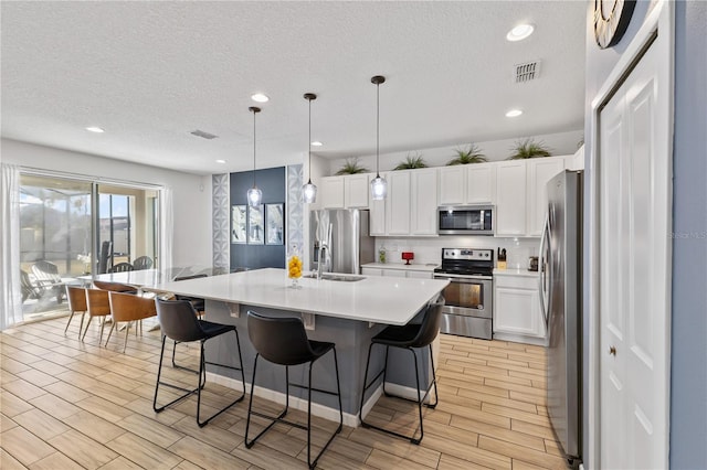 kitchen featuring an island with sink, white cabinetry, hanging light fixtures, and stainless steel appliances