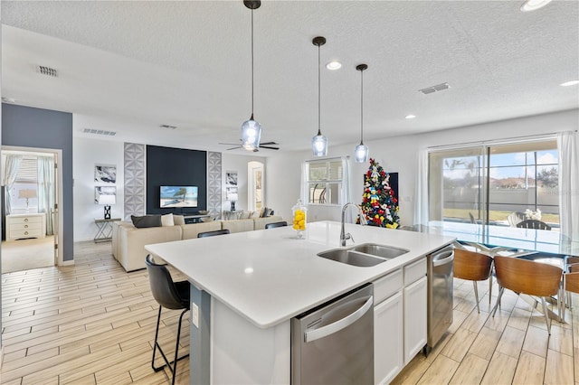 kitchen with stainless steel dishwasher, pendant lighting, sink, white cabinetry, and a kitchen island with sink