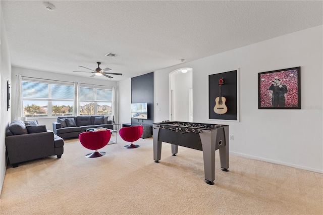 recreation room featuring light carpet, ceiling fan, and a textured ceiling