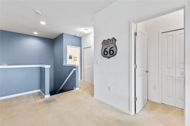 corridor with a textured ceiling and light carpet