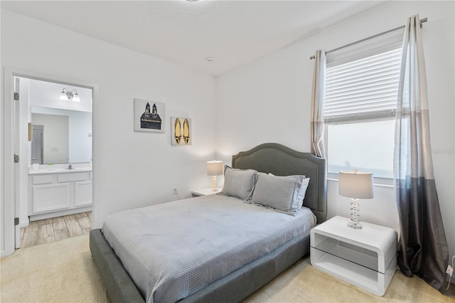 bedroom with sink, multiple windows, light carpet, and ensuite bath