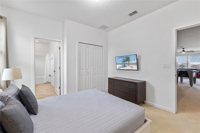 bedroom featuring ensuite bathroom, a textured ceiling, and light carpet