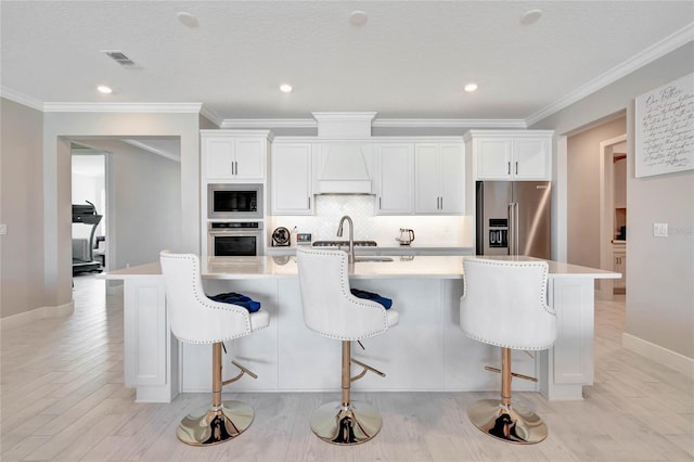 kitchen with appliances with stainless steel finishes, a center island with sink, and white cabinets