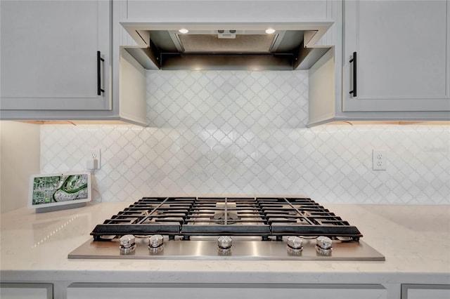 kitchen featuring decorative backsplash, stainless steel gas stovetop, light stone countertops, and custom exhaust hood